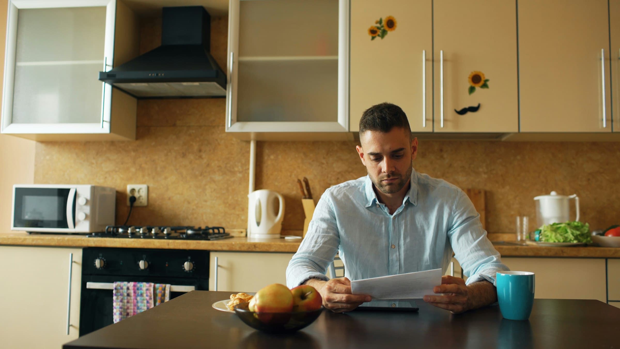 A man at a kitchen table reading a letter early in the morning